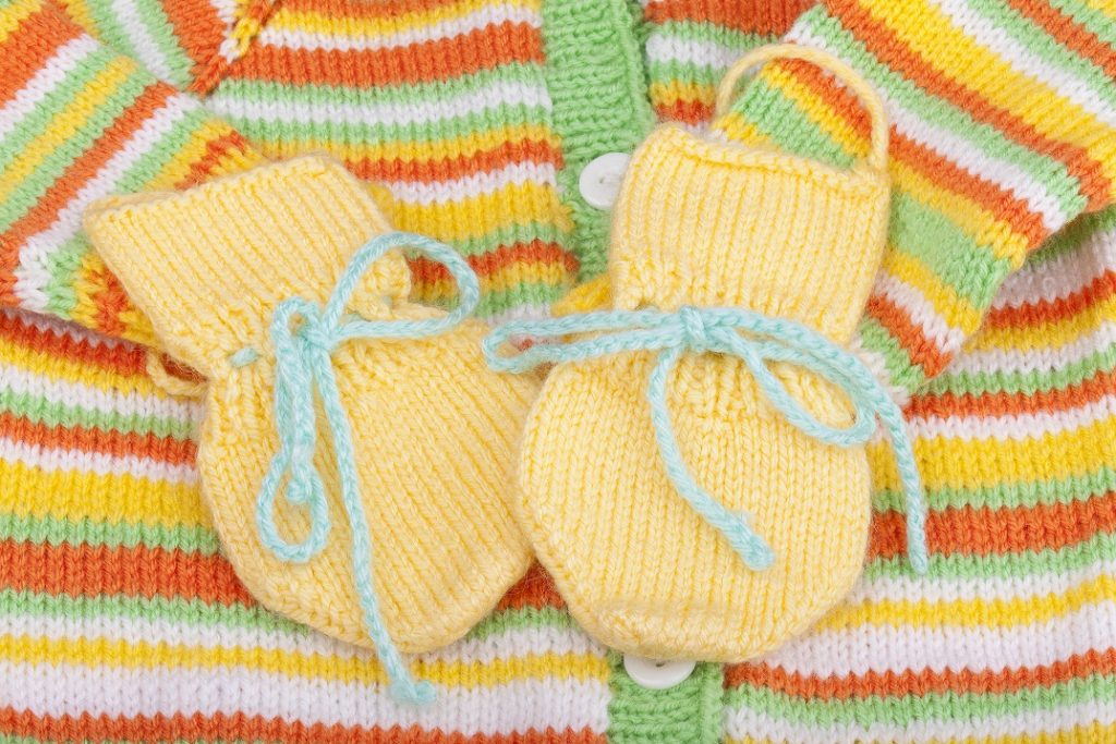 Babysachen selberstricken - gerade in den letzten Wochen der Schwangerschaft hat man dazu häufig Zeit. Hier: handgestrickte Babyhandschuhe auf einer selbstgestickten Babyweste. (#01)